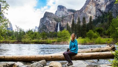 woman sitting on a log with water and mountains in the background