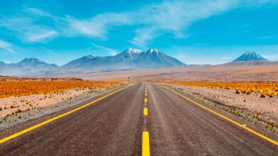 A wide open road in the desert with a bright blue sky and mountains in the distance